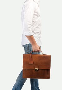 Braune Lederaktentasche mit flachem Design, rechteckiger Form, angehängtem Etikett und Metallverschluss. Wird in einer Hand getragen und zeigt eine glatte Oberfläche.