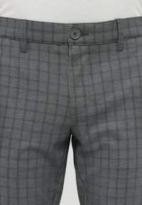 Pantalones de cuadros gris con un patrón de cuadros fino, hechos de tela texturizada. Presentan un cierre de botón y trabillas para cinturón en la cintura.