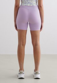 Purple stretch shorts with a mid-rise waistband, smooth texture, and fitted design, paired with white athletic shoes.