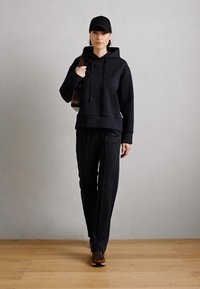 Black hooded sweatshirt with drawstrings, paired with black trousers. Finished with a black cap and brown sneakers. Simple fabric texture.