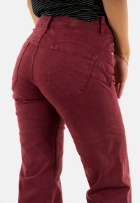 Pantalones granates de tela suave, con dos bolsillos traseros, detalles texturizados a lo largo de la cinturilla y una silueta ajustada.