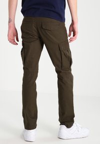 Olivgrön cargobyxor med flera sidofickor, smalnade ben och ett hållbart tyg. Bärs med vita sneakers. Enkelt mönster.