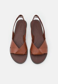 Sandales en cuir marron avec un design à lanières croisées, dos ouvert et semelles rembourrées. Texture lisse avec une base robuste et flexible. Ajustement réglable.