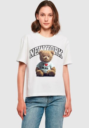 T-shirt en coton blanc présentant un graphique d'un ours en peluche portant une chemise bleue avec "I ♥ NYC" et un texte en gras "NEW YORK" au-dessus.