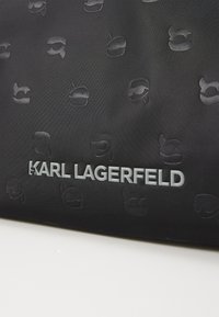 Juodas audinio maišelis, papuoštas įspaustu logotipų siluetų raštu, su išryškintu sidabriniu „KARL LAGERFELD“ prekės ženklu priekyje.