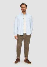 Lichtblauw geruit overhemd met button-down kraag over een wit T-shirt, gecombineerd met bruine corduroy broek en bruine sneakers.