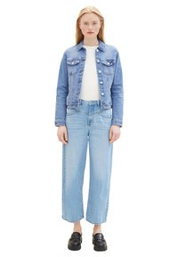 Chaqueta de mezclilla azul claro con dos bolsillos en el pecho, camiseta blanca debajo y vaqueros de pierna ancha en azul claro. Un par de zapatos de plataforma negros completa el conjunto.