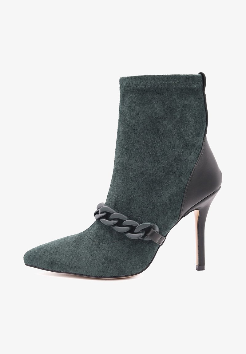 Bottine en suède vert avec un bout pointu, des accents en cuir noir et une chaîne décorative grise sur le devant. Design à talon aiguille.