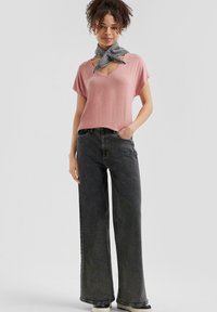 Atasan lengan pendek berwarna merah muda dengan kerah V, dipadukan dengan celana jeans hitam longgar yang memiliki pinggang tinggi. Penampilan ini dilengkapi dengan scarf abu-abu yang diikat di leher.