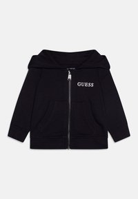 Černá zipová mikina z bavlny s přední kapsou, kapucí a bílým logem "GUESS" na hrudi. Má žebrované manžety a lem.