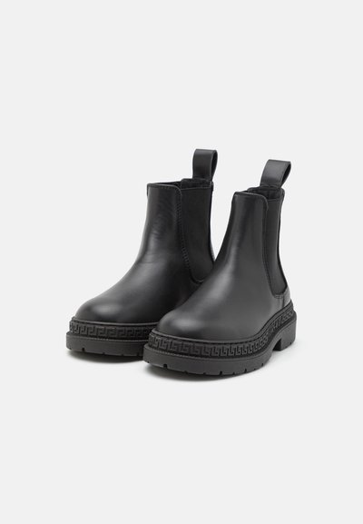 Botas Chelsea de cuero negro con paneles laterales elásticos y tiradores, que presentan una suela de goma texturizada con un borde estampado.