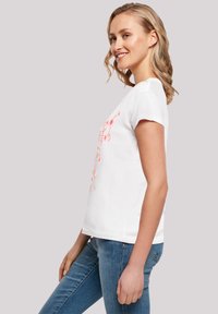 White cotton t-shirt with short sleeves and a crew neckline, featuring a pink graphic design on the front. Paired with blue jeans.
