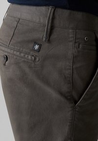 Chinos gris foncé en mélange de coton, avec une fermeture à bouton, des poches latérales et une petite étiquette logo près de la poche arrière.
