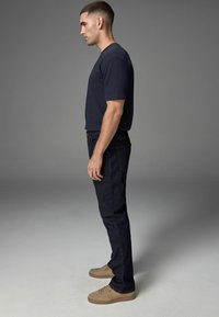 Marineblaues Kurzarmhemd, dunkle Jeans, beige Sneakers. Das Hemd hat eine gerippte Textur; die Jeans verfügen über Gesäßtaschen und eine schmale Passform.
