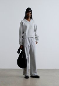 Vaaleanharmaa, väljä collegepaita ja siihen sopivat housut, jotka on valmistettu pehmeästä materiaalista. Musta pipo ja musta laukku, sekä tasapohjaiset kengät. Minimalistinen design.