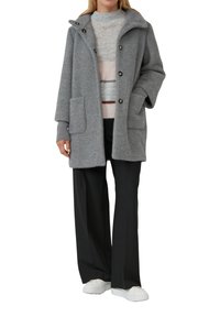 Grau herringbone-Mantel mit Kapuze, zwei Fronttaschen und braunen Knöpfen, über einem leichten Pullover getragen und kombiniert mit schwarzen Hosen.