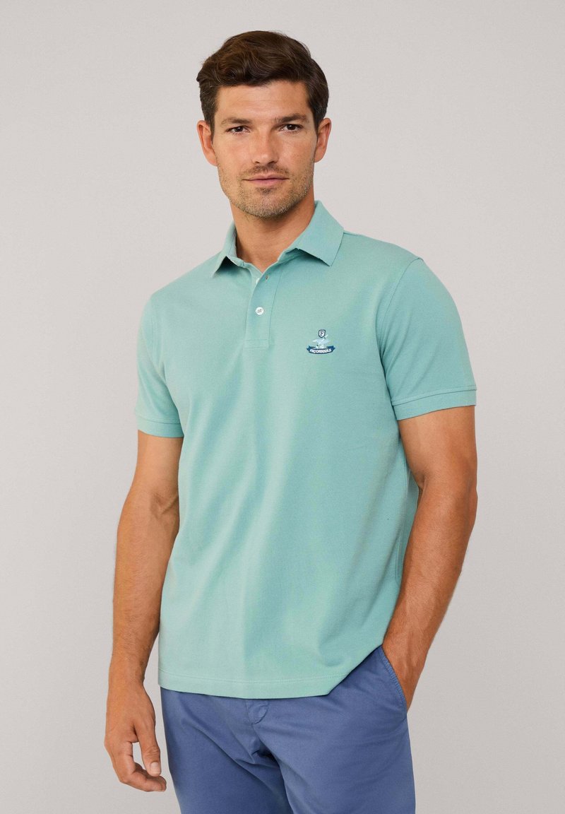 Polo en vert menthe clair avec des manches courtes, col boutonné et logo brodé sur la poitrine gauche. Matière en coton doux.