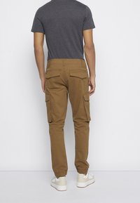 Brune cargo bukser med tætsiddende ben, elastiske manchetter og sidelommer. Båret med en grå T-shirt med korte ærmer og hvide sneakers.