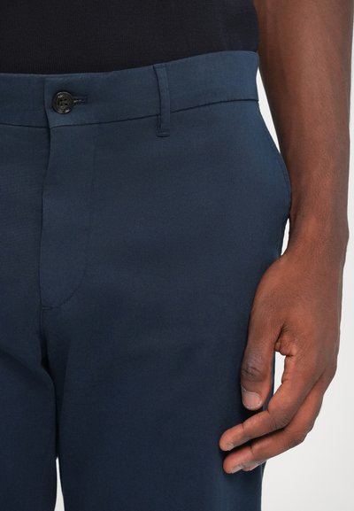Navy blue trousers made of a smooth, woven fabric with a button closure at the waist and a front pocket. Visible stitching details.