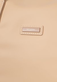 Borsa beige realizzata in materiale sintetico liscio. Presenta una placca rettangolare con testo in rilievo e cuciture a contrasto lungo i bordi.