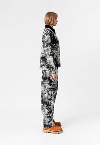 Conjunto de chaqueta y pantalones de tela con un patrón en blanco y negro, con un acabado texturizado; unos zapatos naranjas de suela gruesa completan el atuendo.