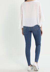 Top in chiffon bianco con maniche a campana abbinato a jeans skinny blu e sneakers bianche. Il top presenta una vestibilità ampia e un tessuto testurizzato.