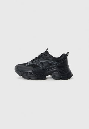 Black athletic shoes with a mesh upper and synthetic overlays, featuring a thick, textured sole with a distinctive tread pattern.