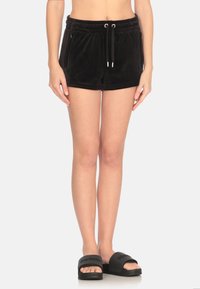 Pantaloni corti neri in velluto con vita elastica, chiusura con cordoncino e due tasche laterali con zip. Abbinati a sandali neri con la pianta piatta.