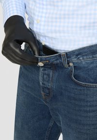 Dark blue denim jeans with a classic design, featuring a metal button closure and contrast stitching. Worn with a light blue checkered shirt.