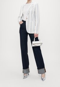 Striped white blazer, light fabric, blue accents; paired with dark jeans featuring folded cuffs, silver high heels, and a white handbag.