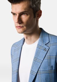 Jasnoniebieska marynarka w kratę, wykonana z teksturowanej tkaniny, z jednorzędowym zapięciem i nowoczesną przypinką z logo na klapie.