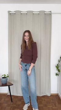 Καφέ ριγωτό μπλουζάκι με μακριά μανίκια, συνδυασμένο με ανοιχτό μπλε παντελόνι σε ίσια γραμμή. Το χαμογελαστό άτομο στέκεται μπροστά από μια ανοιχτό γκρίζα κουρτίνα. Ξύλινο δάπεδο.