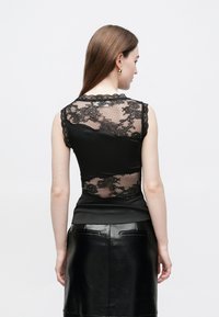 Zwarte mouwloze top met een transparante achterkant van kant, getand kanten randje en een gladde voorkant, gecombineerd met een zwarte leren rok.