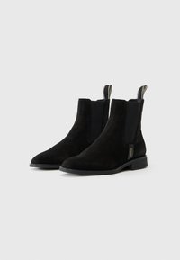 Bottines en suède noir avec des panneaux latéraux en élasthanne, bout arrondi, petit talon empilé et une languette avec un détail de couture contrastante.