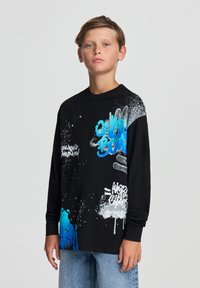 T-shirt a maniche lunghe nera con testo in stile graffiti blu e bianco e motivi di spruzzi. Realizzata in tessuto morbido e liscio. Vestibilità ampia.