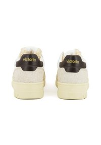 Witte sneakers met een gestructureerde beige achterkant, gouden "victoria" branding op de zwarte hiel tab, en een crèmekleurige rubberen zool.