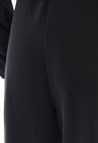 Close-up van een persoon die een nauwsluitende zwarte broek draagt, gemaakt van een gladde, licht rekbare stof.