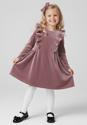 Sukienka z długim rękawem z różowego aksamitu z falbanami, okrągłym dekoltem, rozkloszowanym dołem, połączona z białymi teksturowanymi rajstopami i czarnymi lakierowanymi butami.