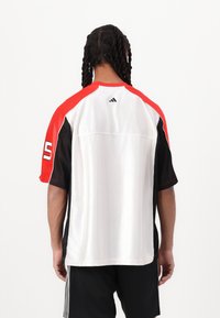Jersey atlético de manga corta con hombros rojos, lados negros y cuerpo blanco. Tejido texturizado con el acento "5" en la manga izquierda.