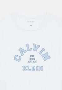 Λευκό βαμβακερό t-shirt με μπλε καμπυλωτή εκτύπωση που γράφει "CALVIN KLEIN CK 205 NY NY" με έντονη γραμματοσειρά. Βραχίονες κοντοί και στρογγυλή λαιμόκοψη.
