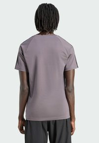 Camiseta atlética corta de manga en morado con cuello redondo, mangas raglán y textura suave. La vista trasera no muestra logotipos ni patrones visibles.