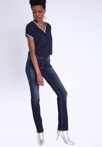 Top navy de manga corta con escote en V y ribete blanco, combinado con unos jeans de mezclilla oscuros y tacones plateados de punta. Tela suave y diseño ajustado.