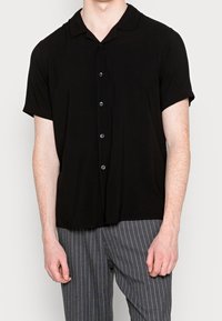 Czarna koszula z krótkim rękawem, kołnierzem typu camp, sześcioma guzikami z przodu i luźnym krojem. Tkanina wydaje się gładka i lekka.