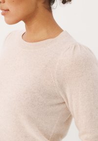 Jasnoróżowy sweter wykonany z miękkiego dzianinowego materiału, z okrągłym dekoltem i bufkami na rękawach z delikatnymi detalami tekstur.