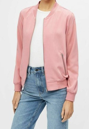 Kobieta w jasnoróżowej bomberce na zamek, na białej koszulce i wysokim stanie jasnoniebieskich dżinsów.