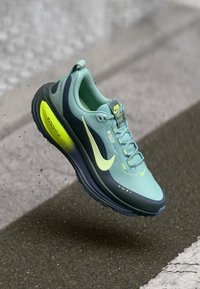 Helle blaue Laufschuhe mit dunkelblauen Akzenten, strukturiertem Mesh-Obermaterial, gelbem Logo und Details, dicker Sohle und Schnürverschluss.