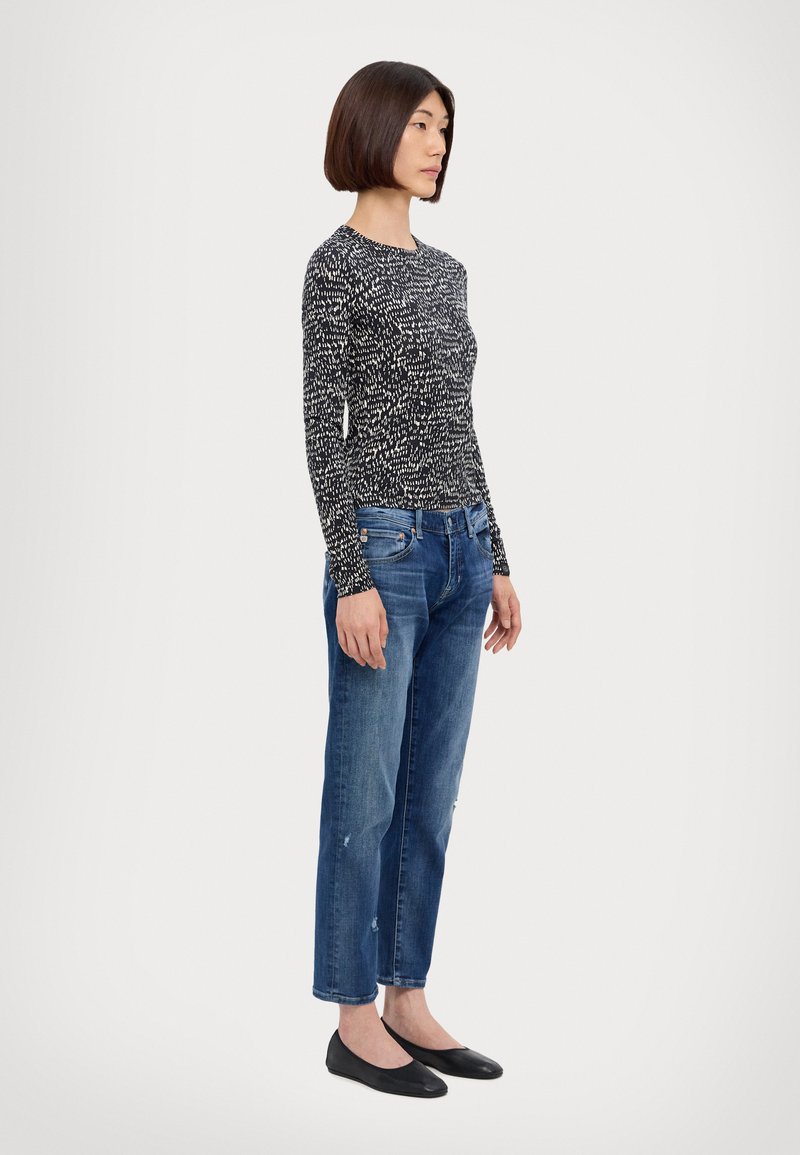 Top cu mânecă lungă, cu model alb și negru, blugi relaxați de culoare albastră și balerini negri. Accentuează elemente de design subtile și texturi.