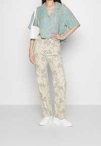 Koszula z krótkim rękawem w jasnoniebiesko-beżowy abstrakcyjny wzór, zestawiona z beżowymi spodniami z konturami dłoni. Całość dopełniają białe trampki.