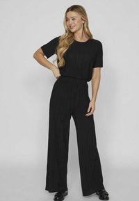 Zwarte geplooide jumpsuit met korte mouwen en een ronde halslijn, met een losse pasvorm en brede pijpen. Textuurstof voegt diepte toe.