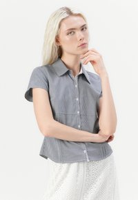 Kortermet skjorte med krage i svart-hvitt ginghammønster, med knapper foran og en lett utvidet nederkant.